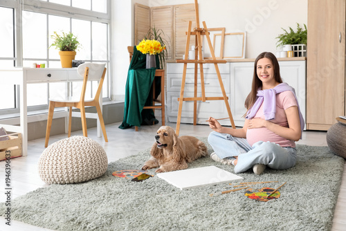 Obraz na plátně Young pregnant artist painting on floor with dog in room