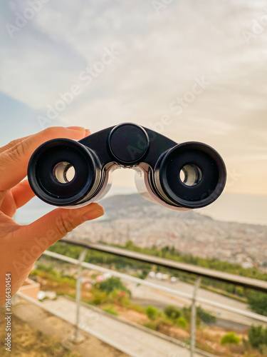 Hands holding binoculars examine the cityscape. Mobile photo