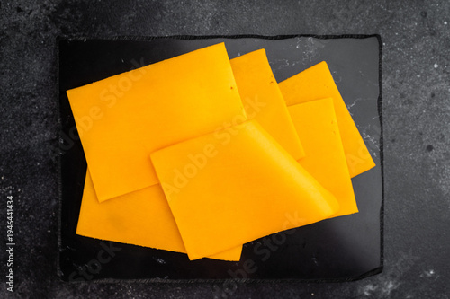 Cuadro en lienzo Stack of orange cheese slices on black stone background minimal food composition
