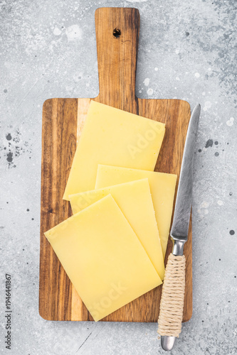Foto Stack of semi hard yellow cheese slices on rustic wooden cutting board, copy spa