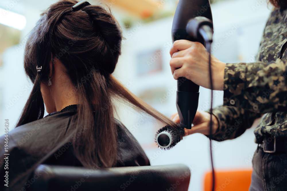 Fototapeta premium Professional Hair Straightening with Brush and Blow Dryer in Salon. Hairdresser straightening client’s hair with round brush and blowdryer, back view