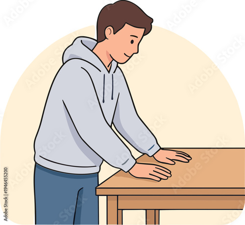 A man in a hoodie leaning on a wooden table indoors.