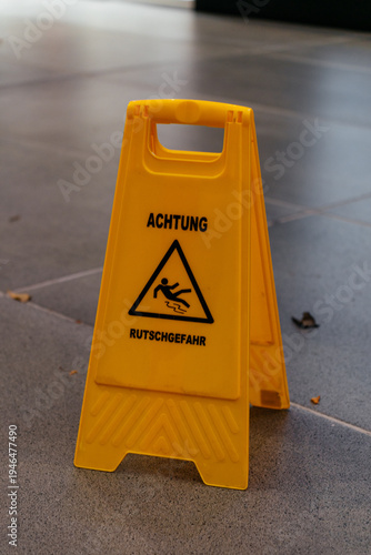 A yellow plastic warning sign on the floor with a German slippery caution message. The image represents safety, risk prevention, and public awareness.