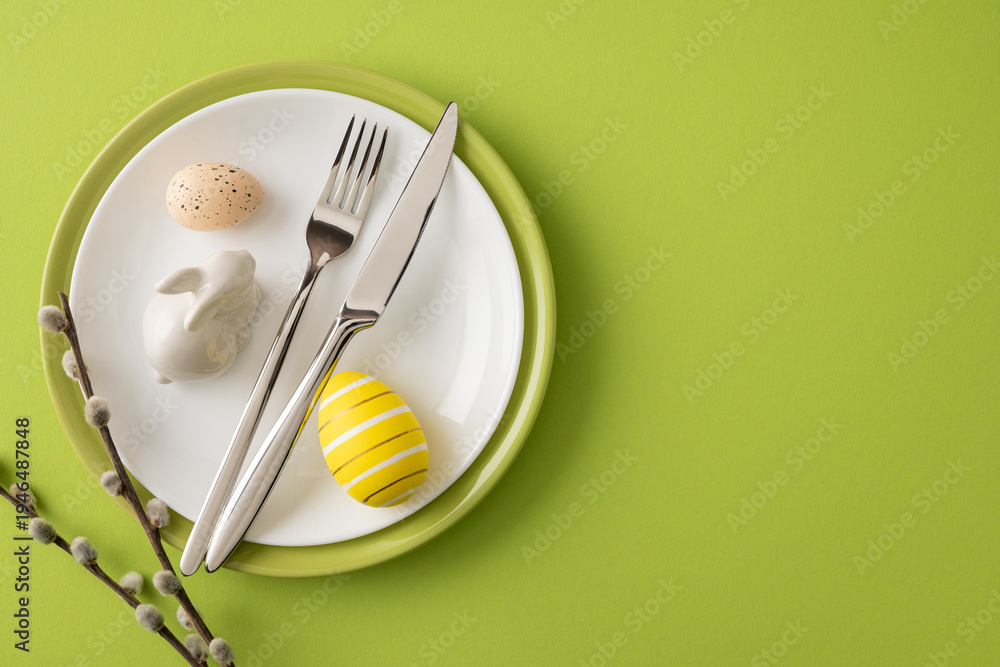 Obraz premium Happy Easter table setting featuring a striped yellow egg, speckled egg, ceramic bunny figurine, silver cutlery and willow sprigs on a green plate and background
