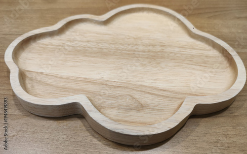 A carved wooden serving plate with decorative shape placed on a table, representing rustic restaurant tableware and antique-style food presentation