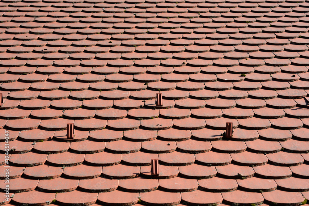 Fototapeta premium A high angle view of red clay roof tiles arranged in a scale pattern featuring small metal snow guards