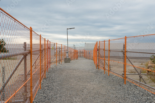 Wallpaper Mural Orange safety fences bordering a gravel path at a construction site under a cloudy sky Torontodigital.ca