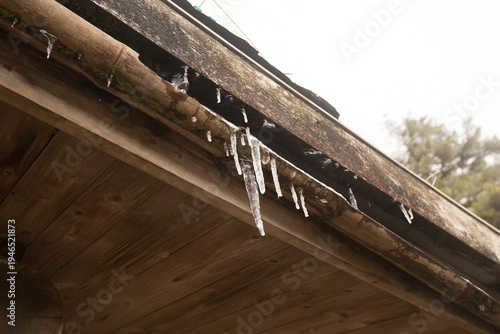 Wallpaper Mural Sharp icicles hanging from a rustic wooden roof under a dramatic cloudy sky Torontodigital.ca