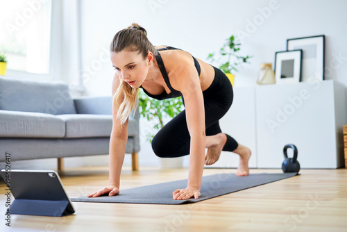 Determined woman learning mountain climber exercise through internet on digital tablet