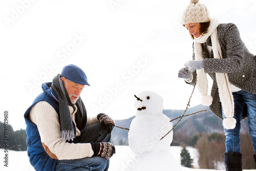 Senior couple building up snowman in winter