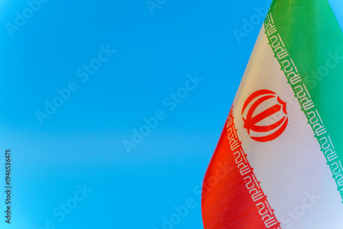 Iran flag against a blue sky background symbolizing political tension and crisis. Close-up view of the Iranian flag representing current geopolitical conflicts, social unrest, and international