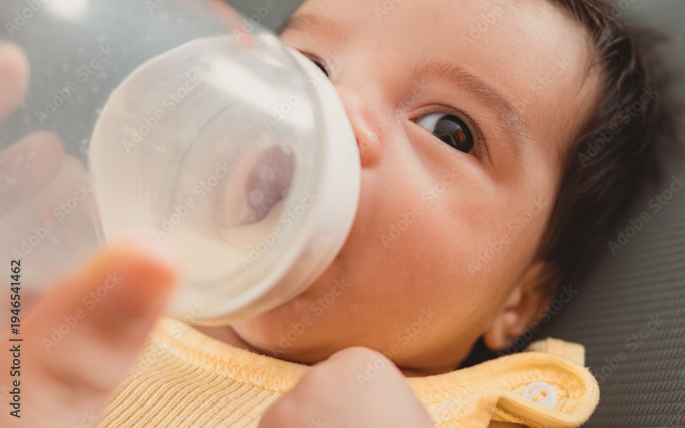 Fototapeta premium Close up of baby drinking milk from a feeding bottle, concept of infant nutrition, newborn care and baby feeding.