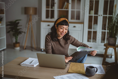 Asian woman working from home using laptop and reading documents
