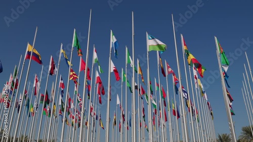 Many international flags waving on tall flagpoles under clear blue sky. Symbol of global cooperation, diplomacy, international relations and unity between countries in modern world.