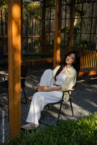Foto Relaxed Asian woman sitting on a chair in a wooden gazebo during sunset