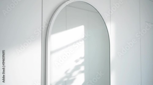 Minimalist arched mirror on white wall with leaf shadows and natural light creates soft interior design concept.