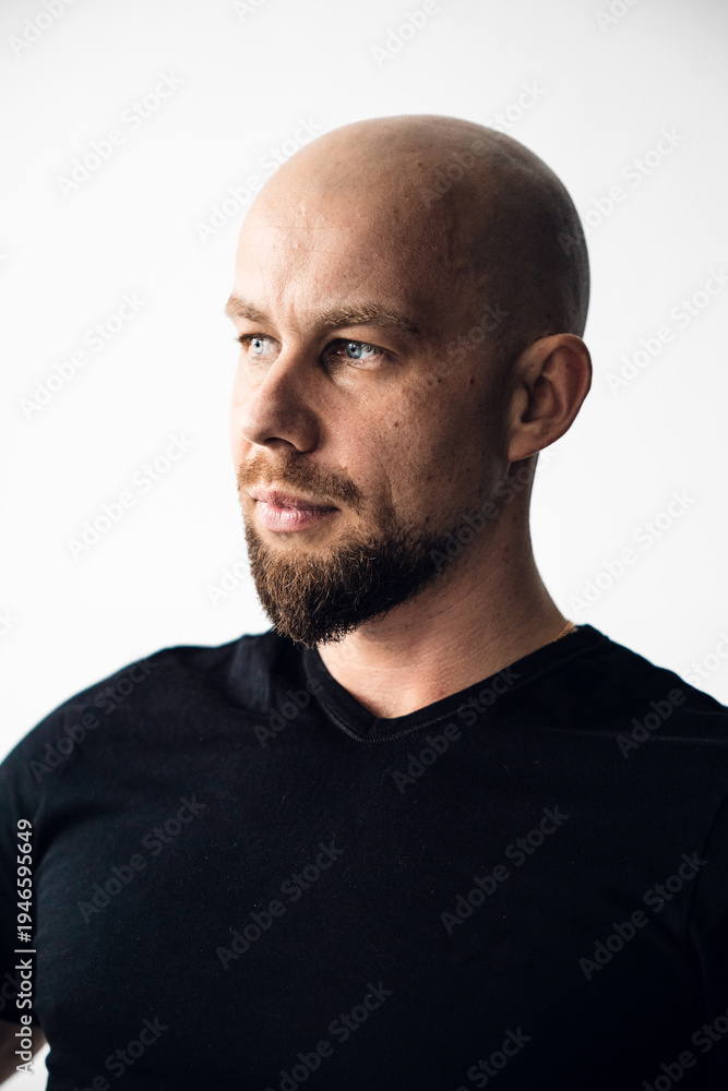 Fototapeta premium Man with bald head and beard looks to the side in bright indoor setting