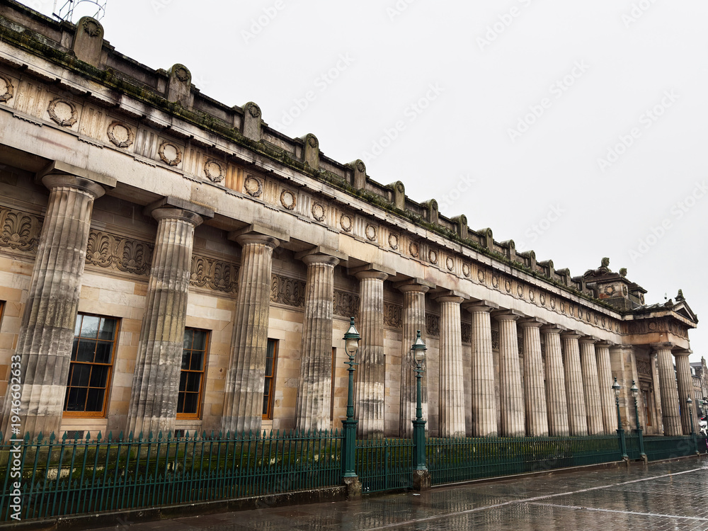 Fototapeta premium Historic neoclassical National Gallery building with grand stone columns and ornate facade in Edinburgh, Scotland, UK on a rainy city street