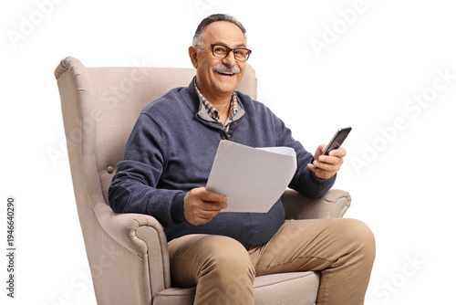 Mature man sitting in an armchair with a phone and a paper document