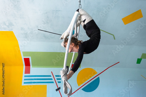 Fotografía Girl performing acrobatic tricks on aerial hoop, elastic bandages for leg safety, gym background, focused circus athlete