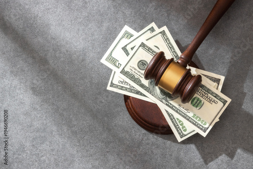 Photos A judge’s gavel lying on scattered US dollar bills and sound block on a gray textured surface, symbolizing financial justice, tax laws legal, penalties or economic law