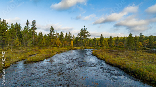 Aerial view of a river snaking through a vibrant landscape with lush trees and a clear sky casting soft shadows, Saariselka, Lappi, Finland.