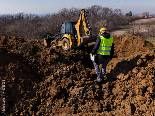 Obraz na plátně Construction engineer supervising backhoe excavation on earthworks site