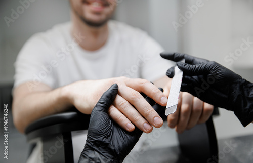 Cuadro en lienzo Manicurist woman using nail file and filing young adult man nails