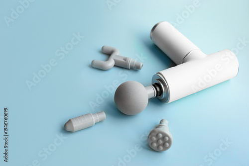 Percussion massage gun with interchangeable heads on blue background, electric muscle massager for recovery and physiotherapy