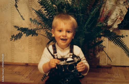 Little boy holding vintage film camera, authentic 1990s family snapshot, retro childhood photography