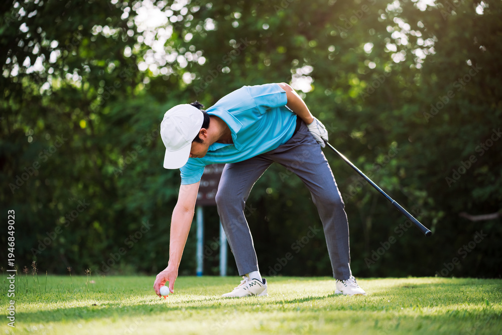 Obraz premium Asian golfer placing golf ball on tee before drive shot at golf course during morning round, preparation and precision in professional outdoor golf sport