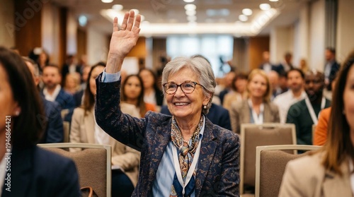 Engaged Audience at the Conference: A distinguished woman, hand raised, participates actively in a conference setting, her bright demeanor reflecting a keen interest in the discourse.
