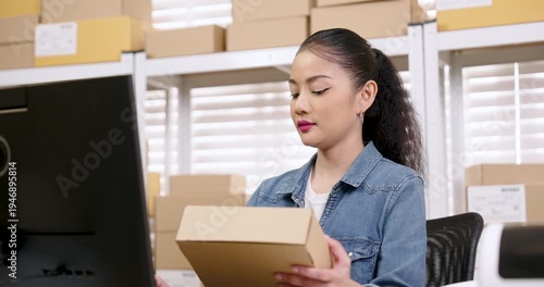 Asian woman small business owner examining parcel box while reviewing order information on screen, checking inventory accuracy, managing e-commerce logistics workflow, preparing online store shipment