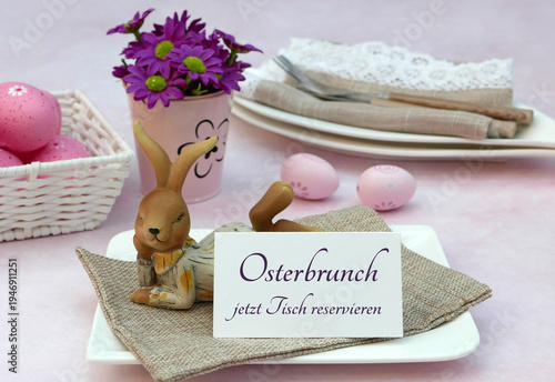 Tischdekoration mit einem Osterhasen, Ostereiern, Besteck auf Stoffserviette und einem Schild mit der Aufschrift Osterbrunch jetzt Tisch reservieren.