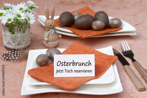 Tischdekoration mit einem braunen Osterhasen, Ostereiern, Besteck auf Stoffserviette und einem Schild mit der Aufschrift Osterbrunch jetzt Tisch reservieren.