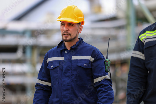 group of industrial engineers workers in a refinery - oil and gas processing equipment and machinery, engineers collaborate with a laptop, blueprint, and digital tablet at the oil storage tanks site.