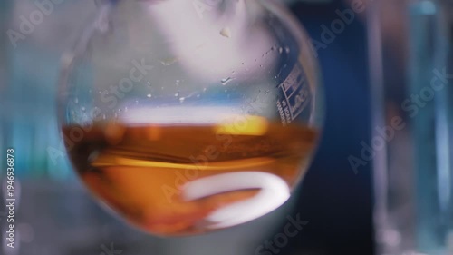 Female researcher preparing a new type of bio fuel. Holding a glass flask with golden liquid close to the camera and swirling the liquid. Selective focus
