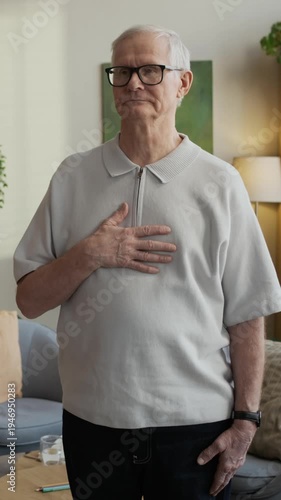 Vertical slowmo shot of senior Caucasian man practicing deep breathing exercise in modern office setting, using mindfulness technique as therapeutic method of coping with stress and anxiety