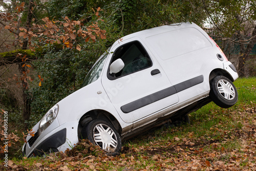 Voiture blanche utilitaire commercial accidentée dans le fossé après une perte de contrôle dans un virage d'une petite route départementale de campagne.