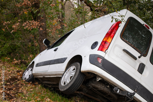 Voiture blanche utilitaire commercial tombée dans le fossé après un accident en dérapage dans un virage d'une petite route départementale de campagne.