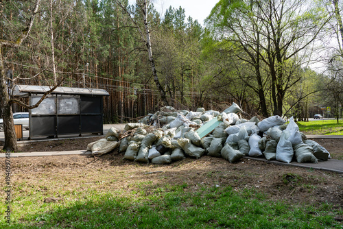 Pile of Garden Waste Bags and Debris Near Park Walkway and Bus Stop in Spring