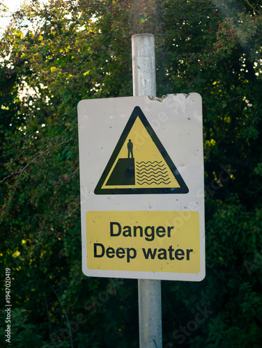 Warning sign for deep water danger with a person standing at the edge, alerting to potential hazards near water bodies.