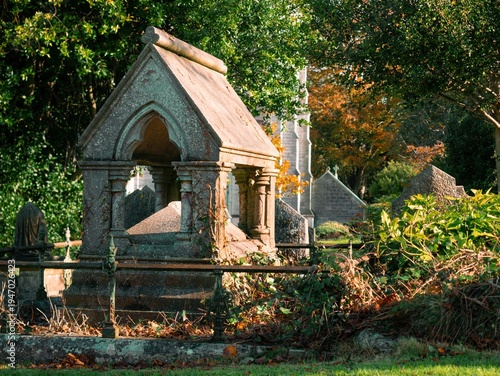 Ancient stone mausoleum in a cemetery, overgrown with ivy, with a church spire in the background