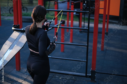 Young female athlete training on outdoor fitness equipment sunny summer day