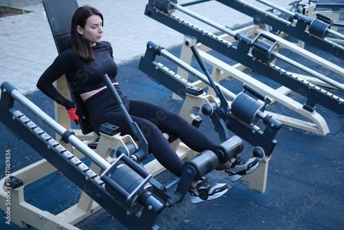 Young female athlete training on outdoor fitness equipment sunny summer day