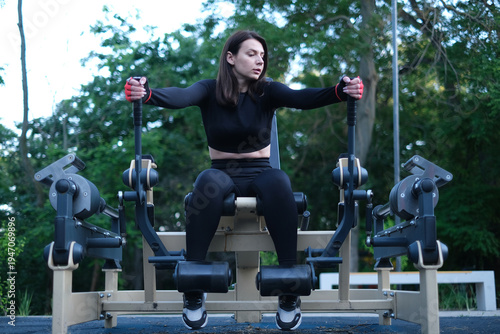 Young female athlete training on outdoor fitness equipment sunny summer day