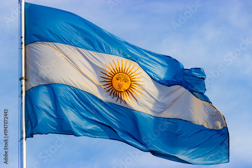 The national flag of Argentina with the Sun of May waving on a flagpole against a clear blue sky.