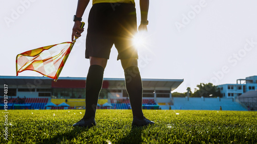Low angle silhouette of a soccer linesman holding a flag against the sun