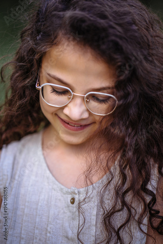 Close up portrait of a smiling young girl with long curly hair and glasses looking down