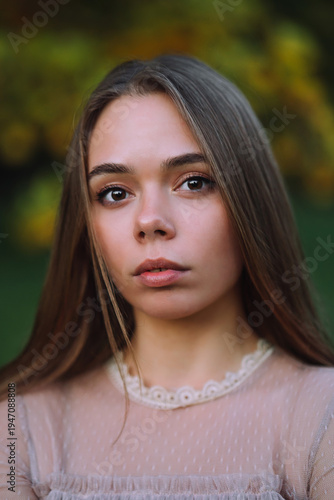 Beautiful young woman with long straight hair looking at camera in autumn park